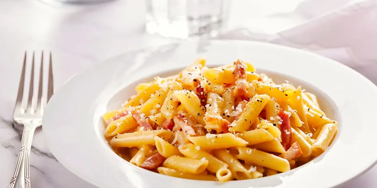 Piatto di pasta penne con speck e zafferano, guarnito con parmigiano e pepe nero.