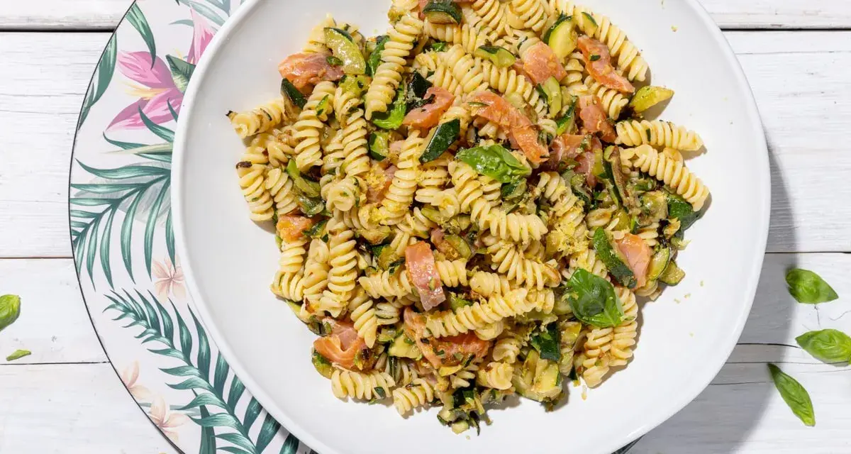 Un piatto invitante di pasta fredda con zucchine e salmone, condita con basilico fresco. Perfetta per un pasto estivo leggero e gustoso.