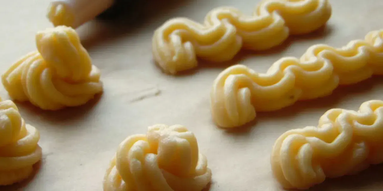 Kremowe eklery z czekoladą i profiteroles w trakcie przygotowania. Widać rękaw cukierniczy i wyciskane ciasto.