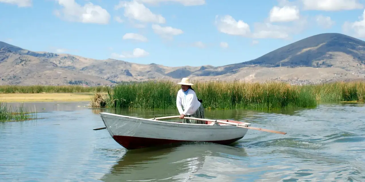 Donna con cappello di paglia rema su un lago, con montagne sullo sfondo. Mete agosto fuori Europa, un'immagine di pace.