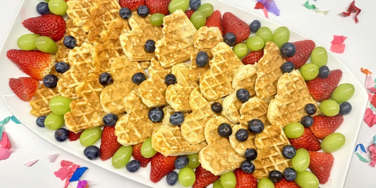 Herzförmige Waffeln mit Erdbeeren, Blaubeeren und grünen Trauben auf einem Teller – ein bunter obstteller kinder für jeden Anlass.