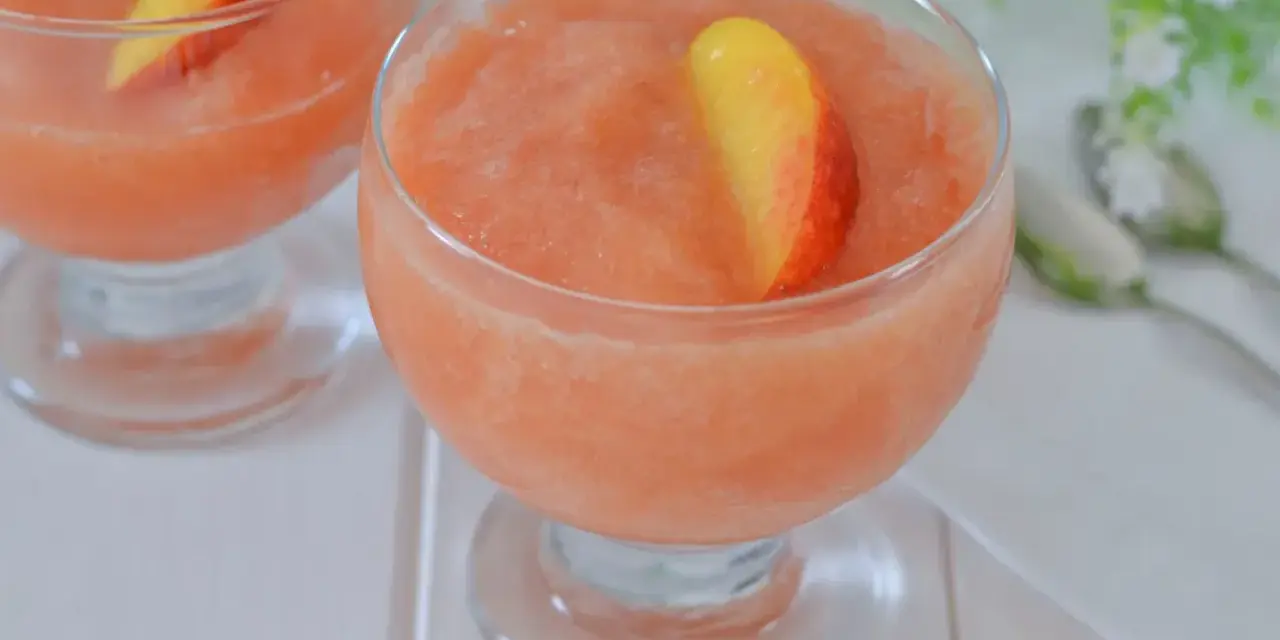 Coppa di granita alla pesca, rinfrescante e dolce, guarnita con una fetta di pesca fresca. Perfetta per un'estate golosa.