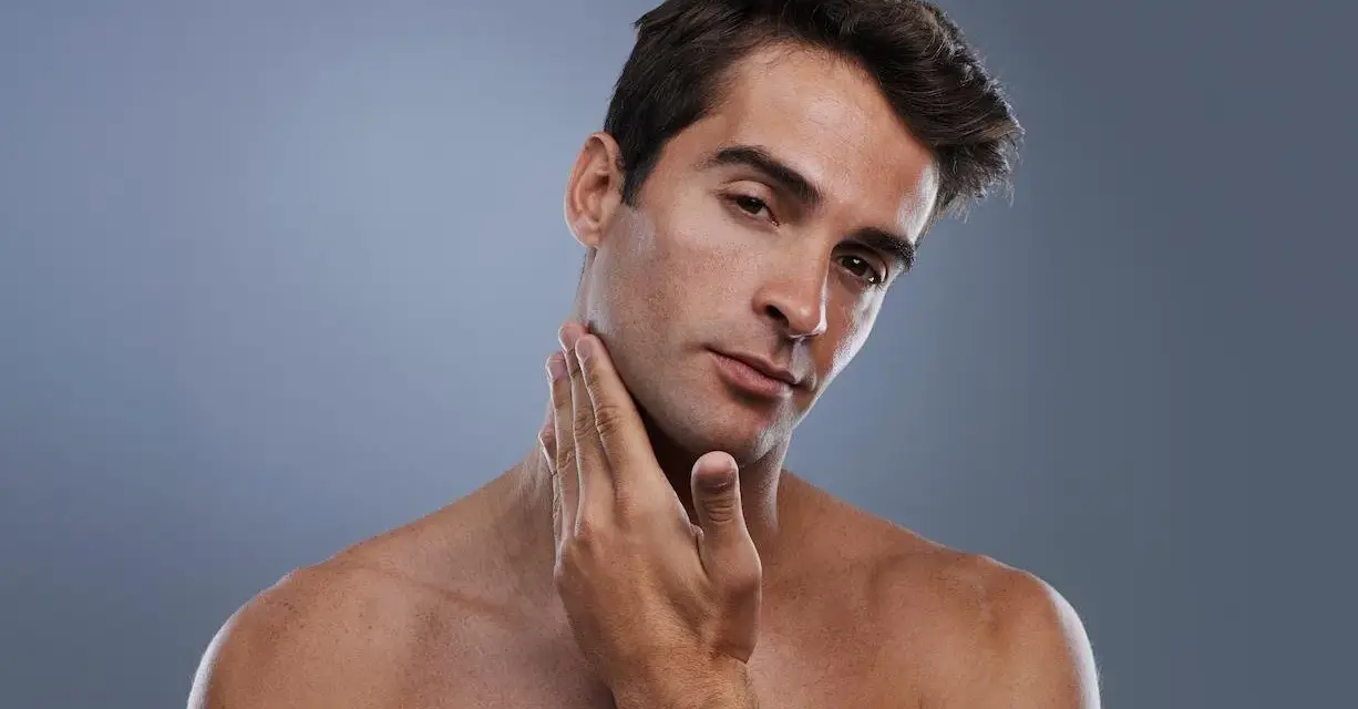 Hombre joven con piel suave y un afeitado perfecto, tocando su mandíbula con la mano.