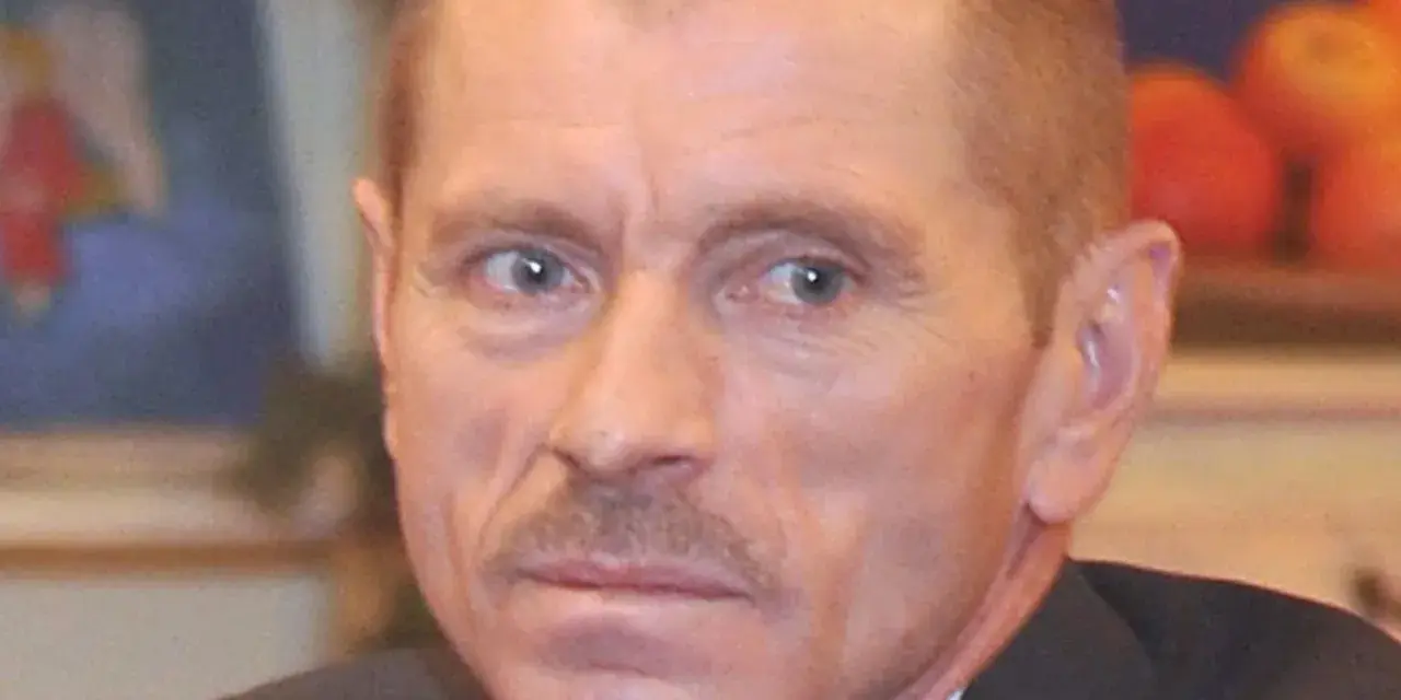 Portret Stanisława Pąka. Mężczyzna z wąsikiem patrzy w bok. W tle owoce.