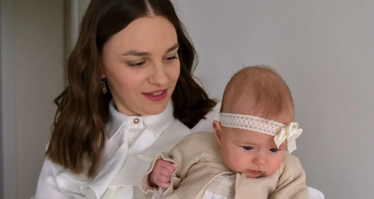 Elegancka mama z niemowlakiem. Inspiracja, jak ubrać się na chrzciny jako gość: biała koszula, subtelne dodatki.