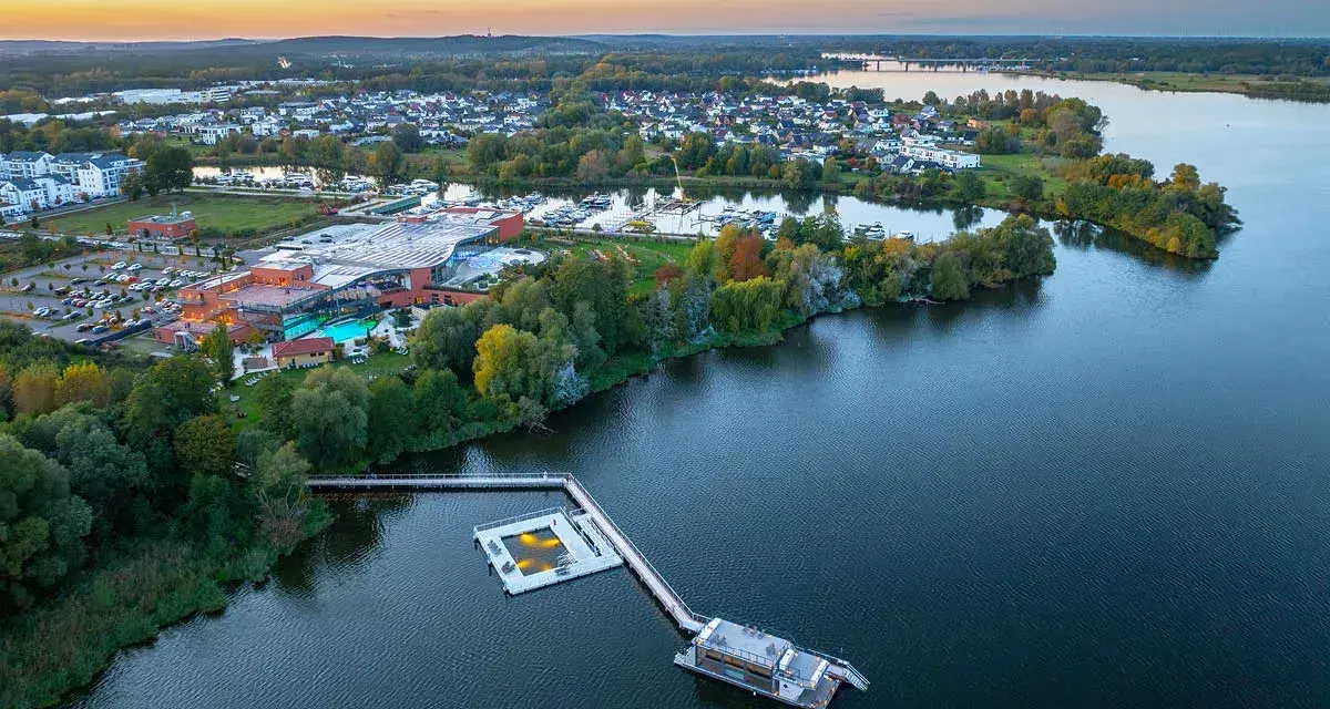 Luftaufnahme der Havel Therme mit einem schwimmenden Pool auf dem Wasser. Ein idyllisches Bild der Entspannung am See.
