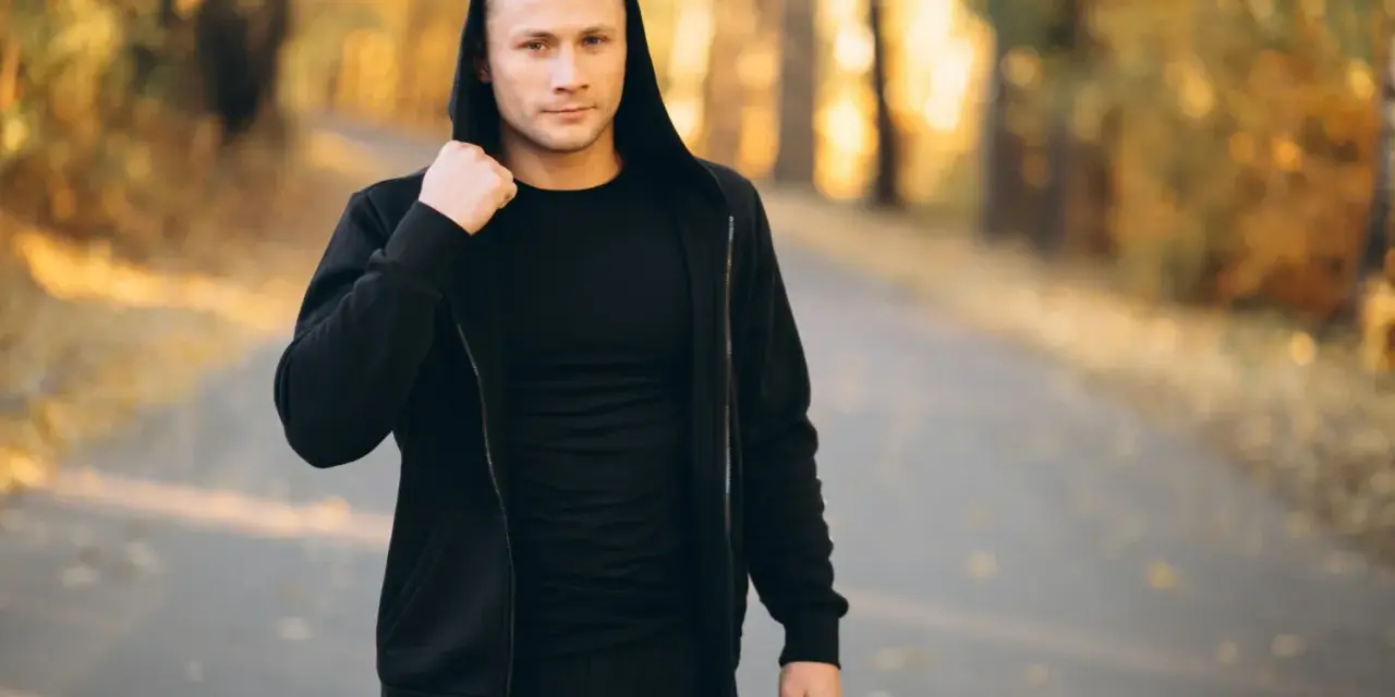 Mężczyzna w czarnej bluzie męskiej Guess z kapturem, stojący na ścieżce w jesiennym parku.