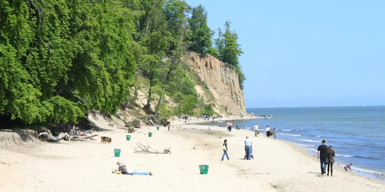 Słoneczny dzień na plaży przy klifie orłowskim. Ludzie spacerują, odpoczywają, a morze spokojnie faluje.