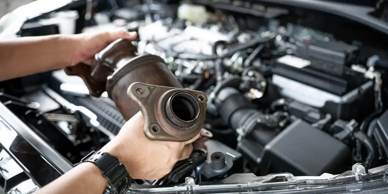 Mechanic holding a catalytic converter, ready for replacement. Understanding the catalytic converter replacement cost is key for car owners.