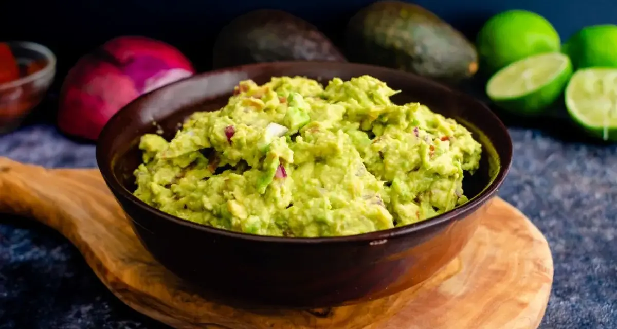 Miseczka guacamole z awokado, cebulą i limonką na drewnianej desce.