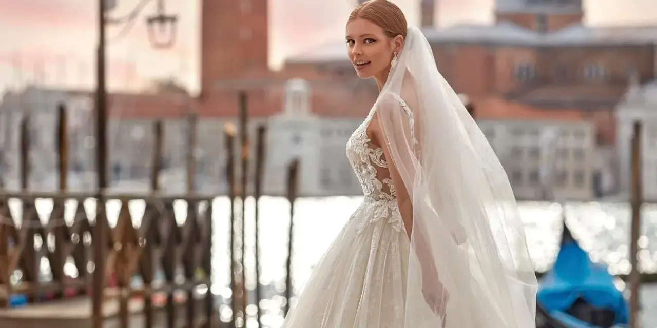 Sposa con abito da sogno e velo svolazzante a Venezia, con gondola blu sullo sfondo. Perfetta per un matrimonio da favola, anche con stivali sposa.