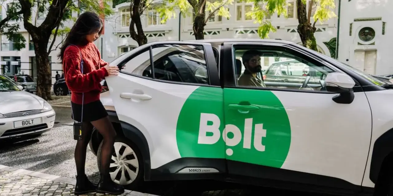 Junge Frau öffnet Tür eines weißen Bolt-Taxis. Fahrer wartet.