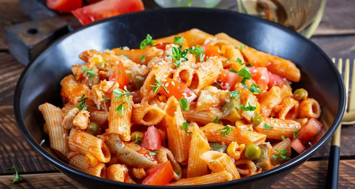 Penne w pikantnym sosie pomidorowym z kawałkami kurczaka, groszkiem i świeżymi ziołami. Danie wygląda jak pyszne spaghetti arrabiata.