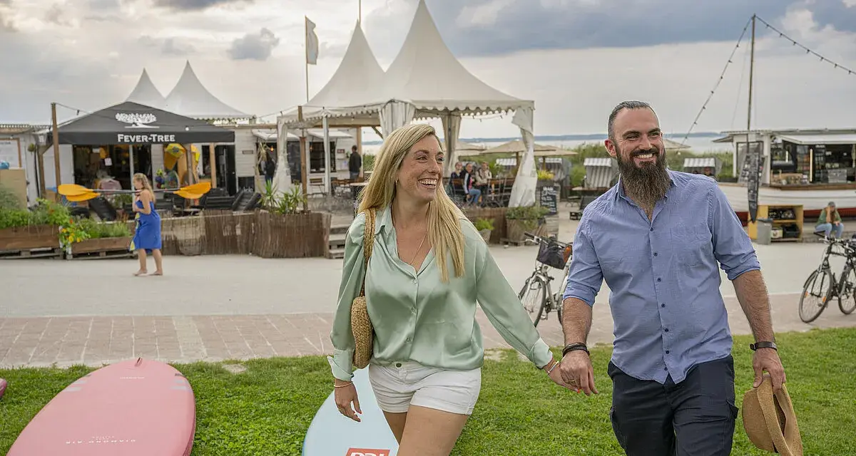 Glückliches Paar spaziert am **Stein Ostsee Strand** entlang, vorbei an SUP-Boards und Strandbuden.