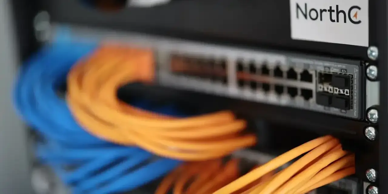 Netzwerkschrank mit blauen und orangen Kabeln, die an einen Switch angeschlossen sind.