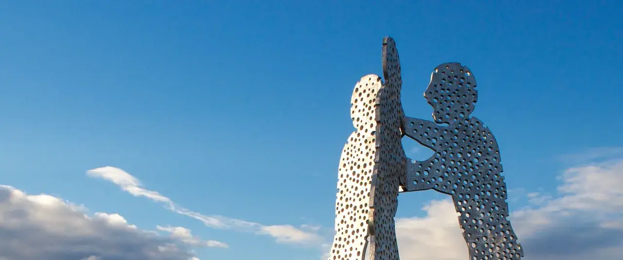 Der Molecule Man in Berlin, eine Skulptur aus Metall mit vielen Löchern, ragt gegen einen blauen Himmel mit Wolken.