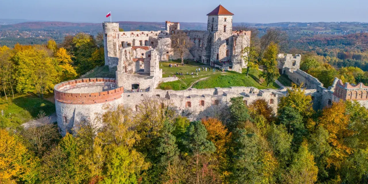 Ruiny zamku na wzgórzu, część szlaku Orlich Gniazd. Jesienne drzewa otaczają kamienne mury.