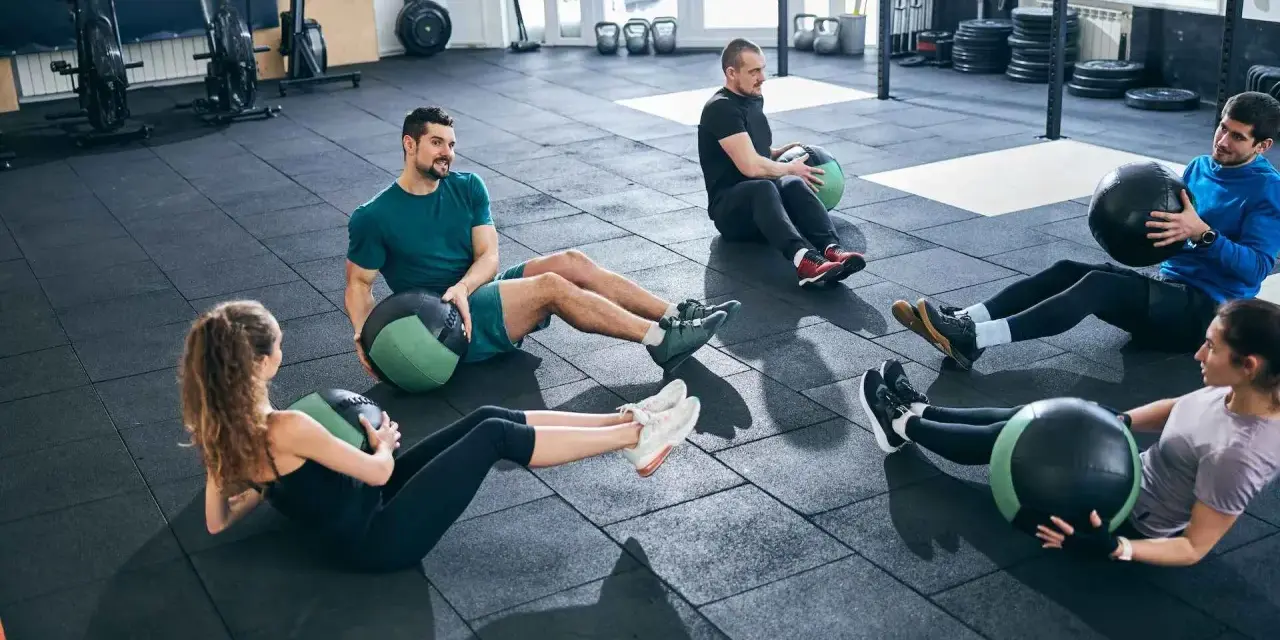 Fünf Personen machen im Fitnessstudio Sit-ups mit Medizinbällen.