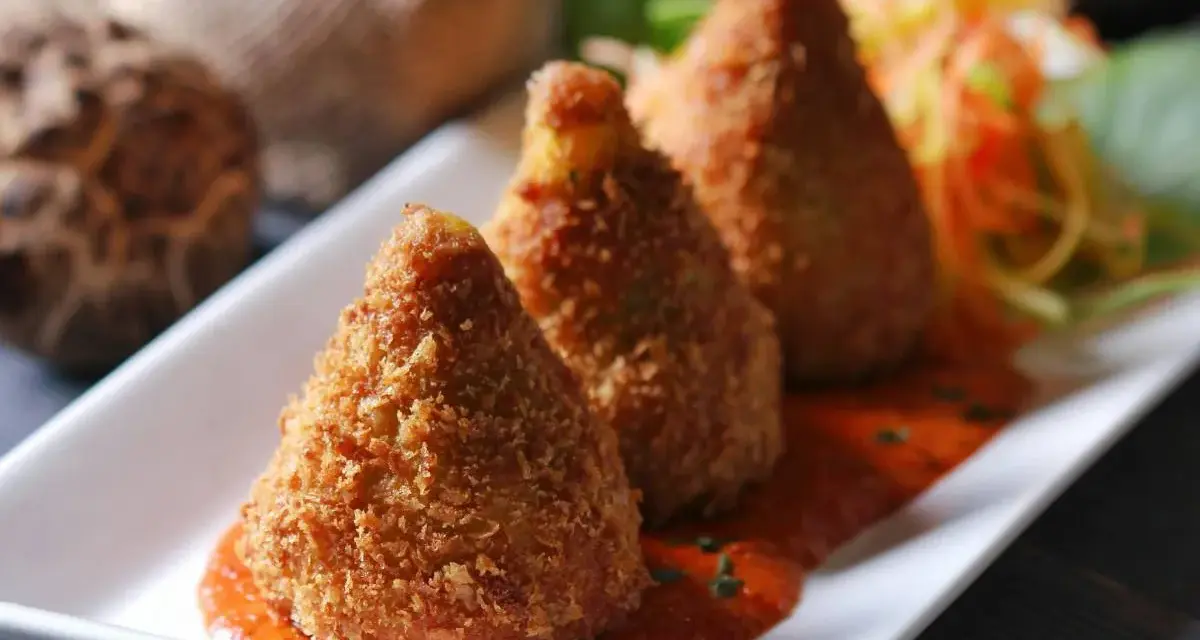 Złociste arancini, idealne do domowego arancini przepis, podane na talerzu z sosem pomidorowym i surówką.