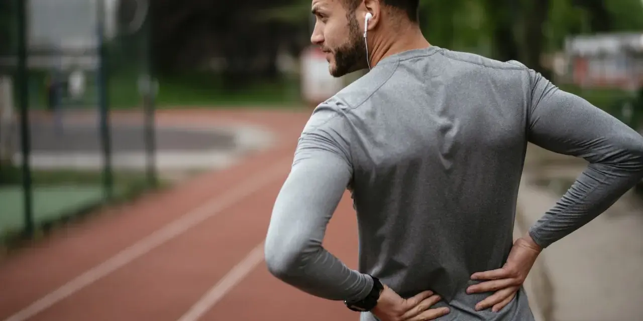 Uomo con le mani sulla schiena, che indica dolore. Forse correre fa male alla schiena, o forse è solo un momento di pausa.