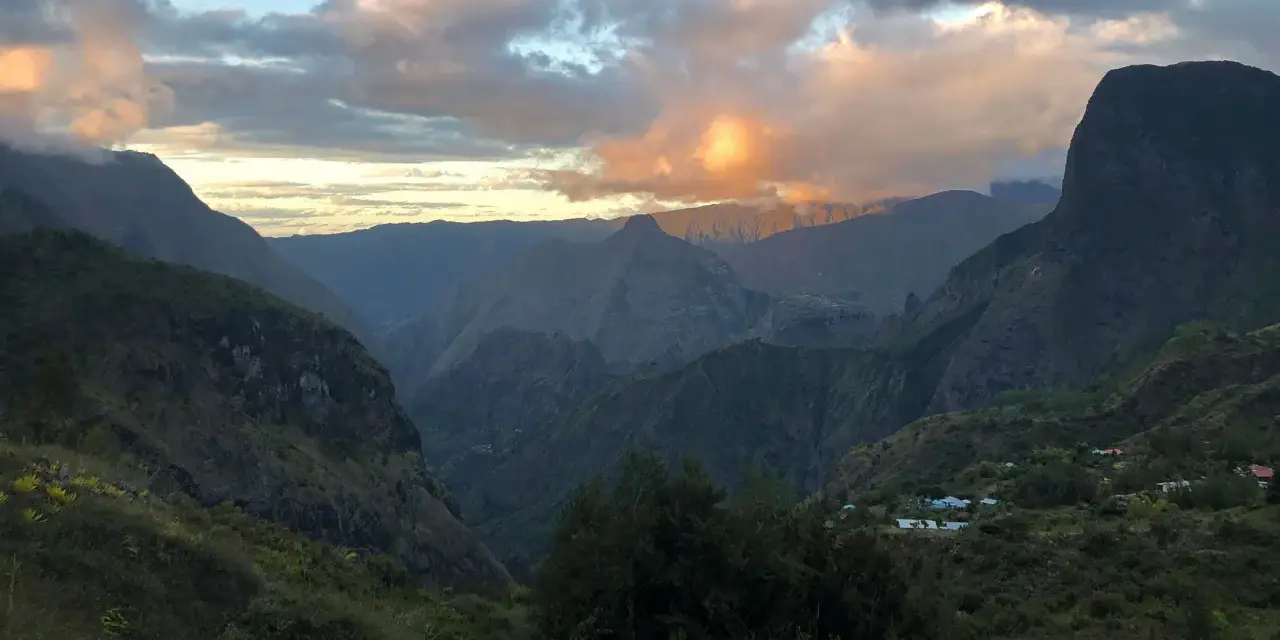 Al tramonto, le montagne della "diagonale des fous" si tingono di rosa. Un villaggio si intravede tra le valli verdi.