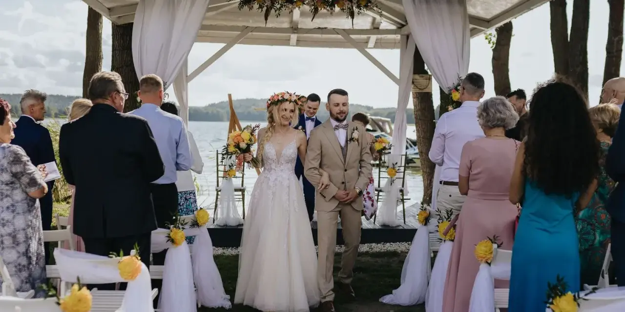 Para młoda idzie do ołtarza. Goście obserwują ceremonię, która może być ślubem cywilnym lub kościelnym.