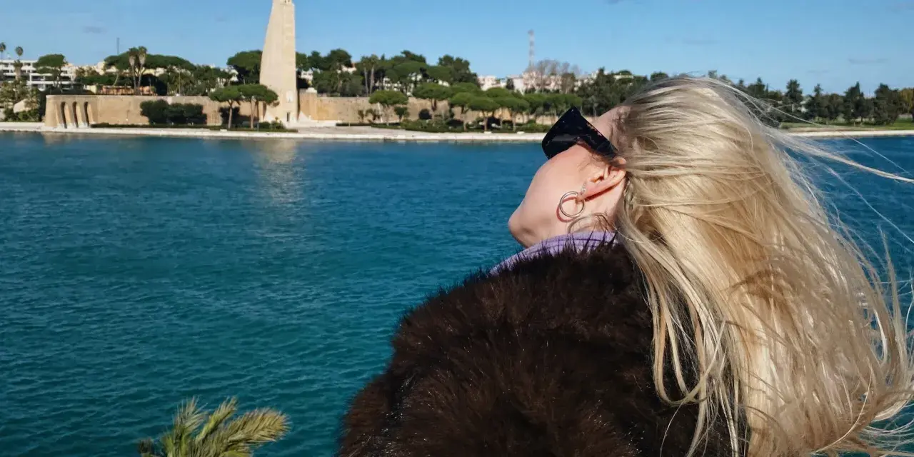 Kobieta z blond włosami podziwia pomnik i morze w Brindisi. Warto zobaczyć to miejsce!
