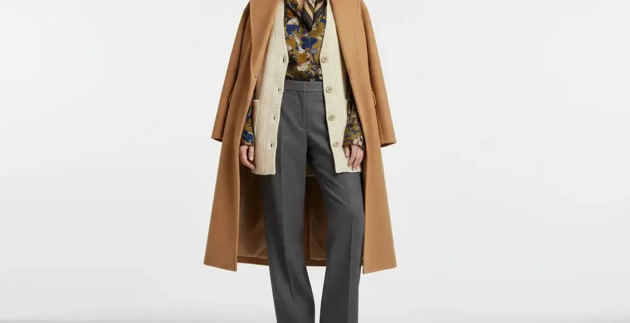 Modello con cappotto cammello, cardigan beige, camicia fantasia, pantaloni grigi e scarpe marroni. Un esempio di vestirsi a cipolla significato per adattarsi a ogni temperatura.