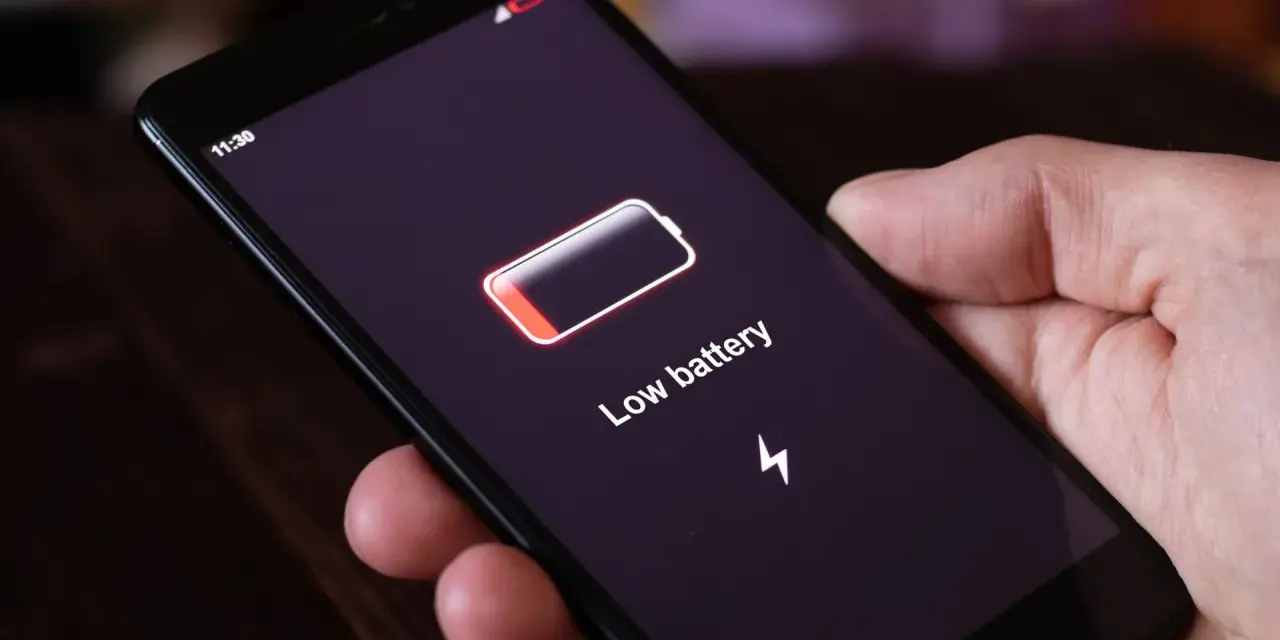 Dłoń trzyma smartfon z komunikatem "Low battery". Czas na naukę, jak oszczędzać baterię w telefonie, by uniknąć takich sytuacji.