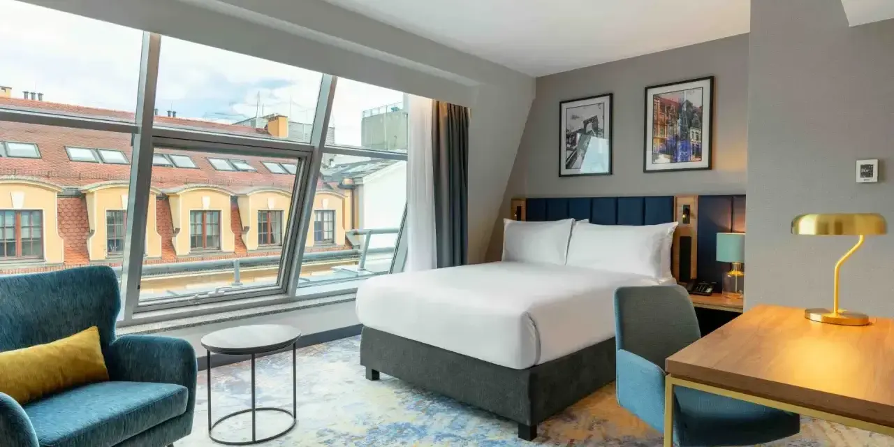 Nowoczesny pokój hotelowy z dużym oknem, łóżkiem i biurkiem. Czy trzeba być pełnoletnim, aby wynająć hotel? Tak, zazwyczaj tak.