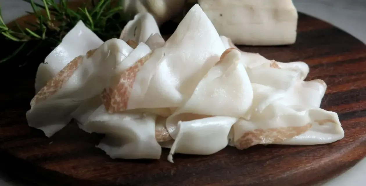 Fette sottili di lardo di Colonnata, profumate con rosmarino e aglio, pronte per essere gustate.