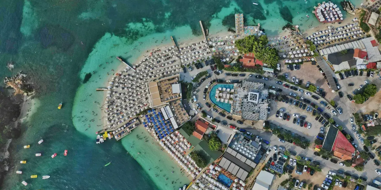 Albania najpiękniejsze miejsca: tętniący życiem kurort plażowy z białymi parasolami, turkusową wodą i basenami.