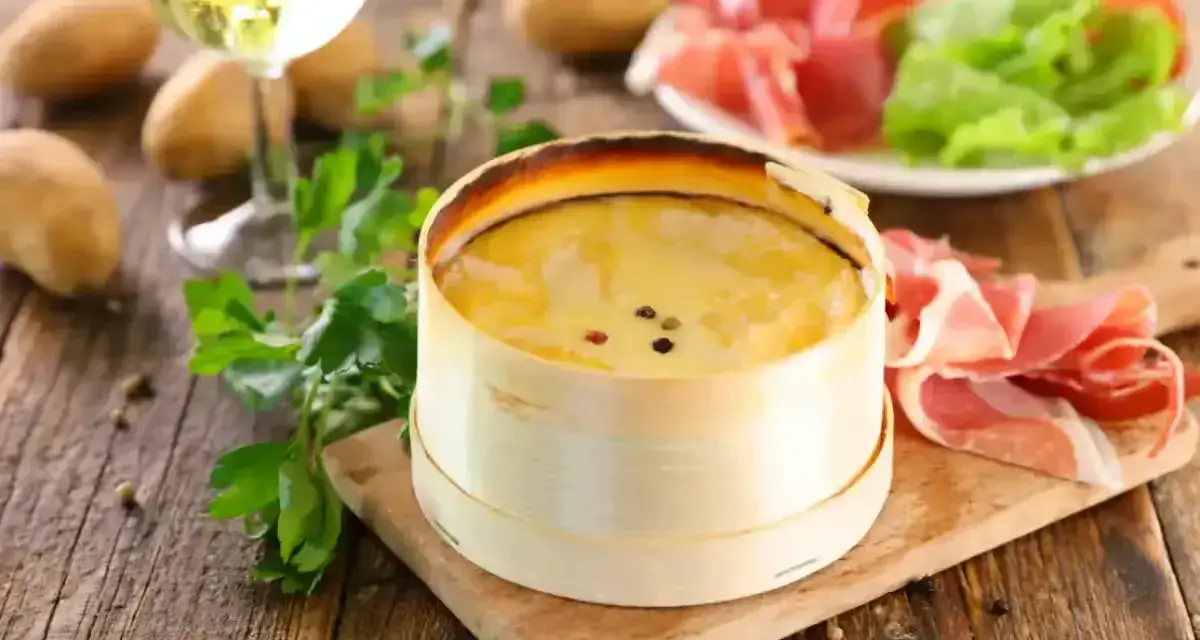 Un délicieux Mont d'Or crémeux, prêt à être dégusté avec du jambon cru, des pommes de terre et un verre de vin blanc.