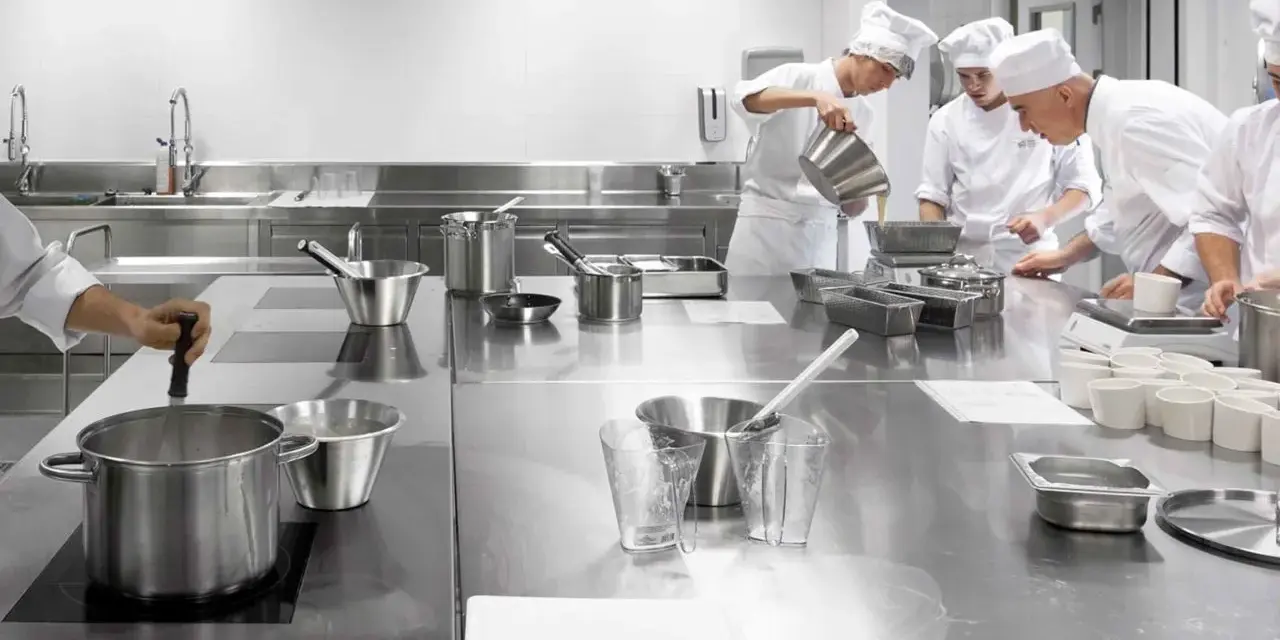 Estudiantes de cocina aprenden sobre seguridad en la cocina, preparando ingredientes en una estación de acero inoxidable.