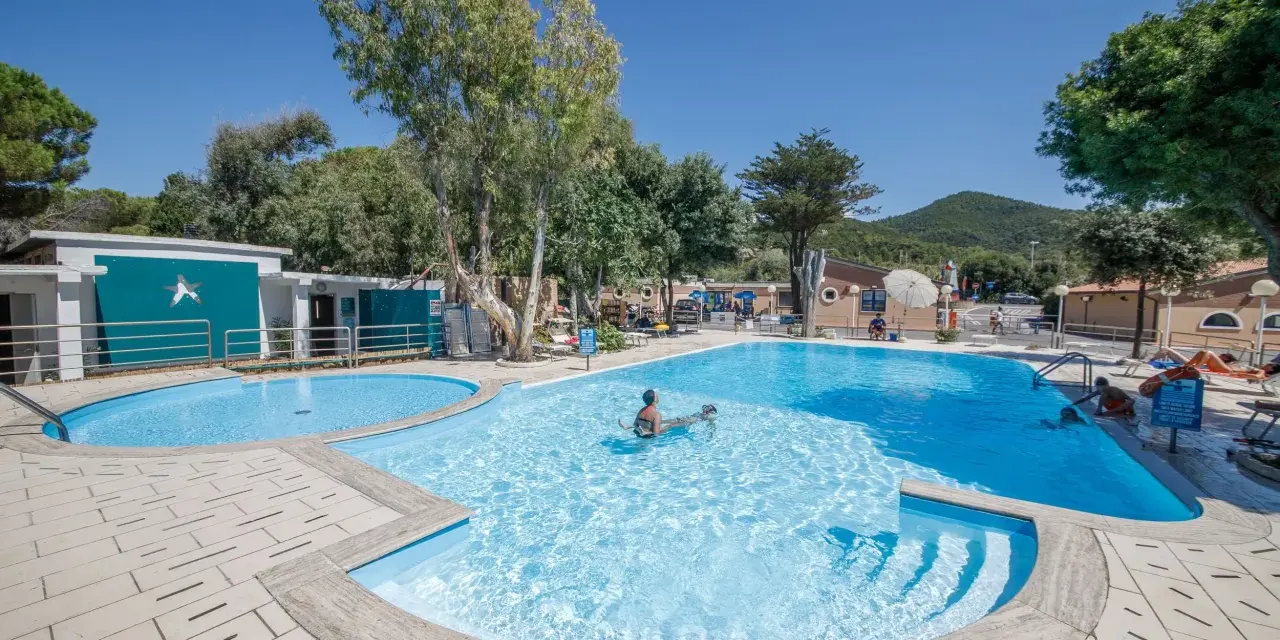 Dzieci pluskają się w basenie na terenie Miramare Camping Village. Słoneczny dzień, błękitne niebo i zieleń drzew tworzą wakacyjny klimat.