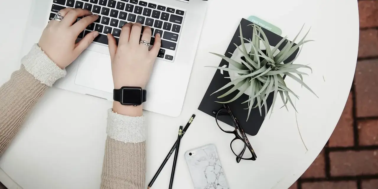 Kobieta pracuje na laptopie, obok leżą okulary, telefon i roślina. To idealne zdjęcia w chmurze do inspiracji.