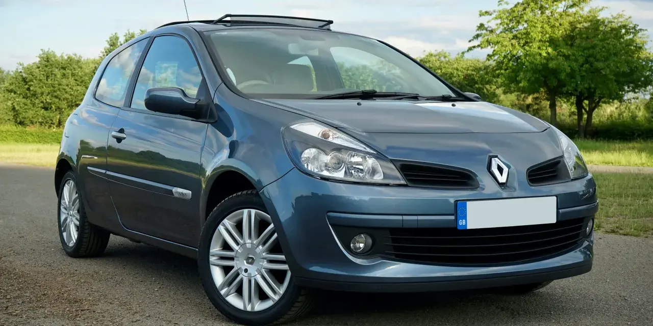 Renault Clio 3 bleue, vue de face, garée sur un chemin de terre.