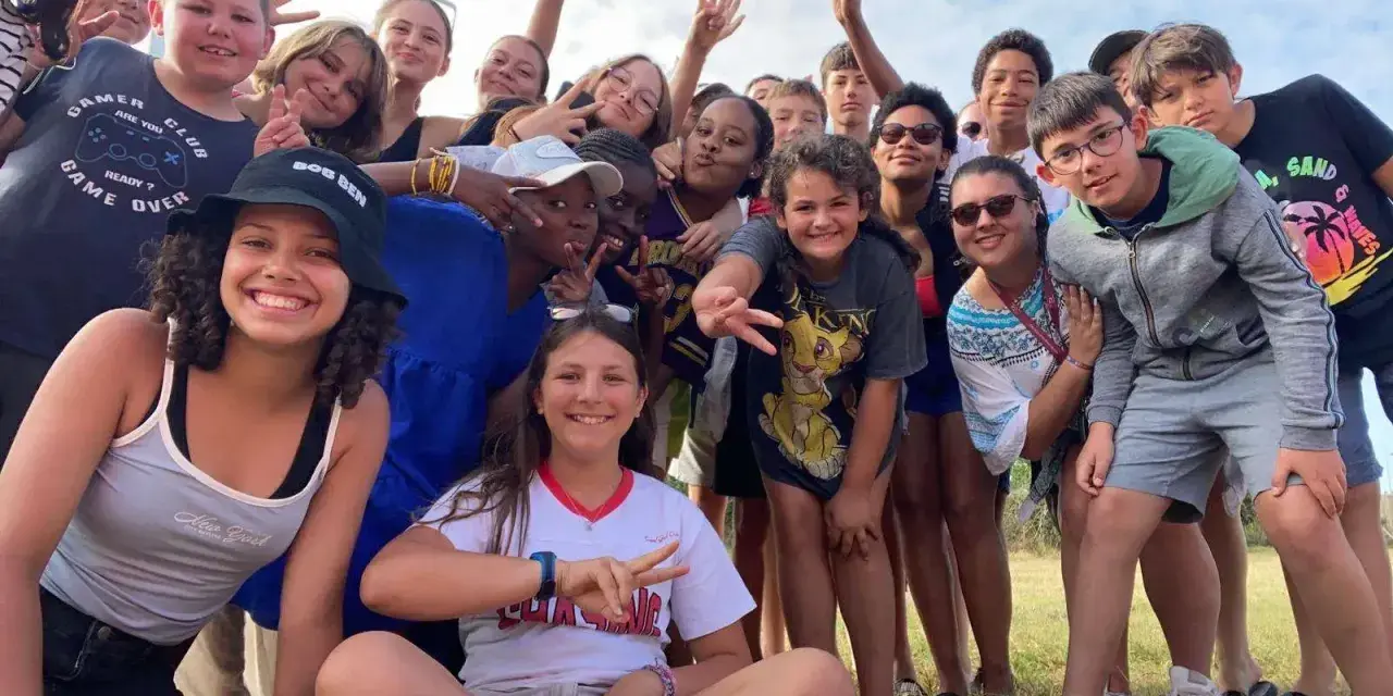 Un groupe d'enfants souriants fait un selfie en plein air, certains faisant le signe de paix.