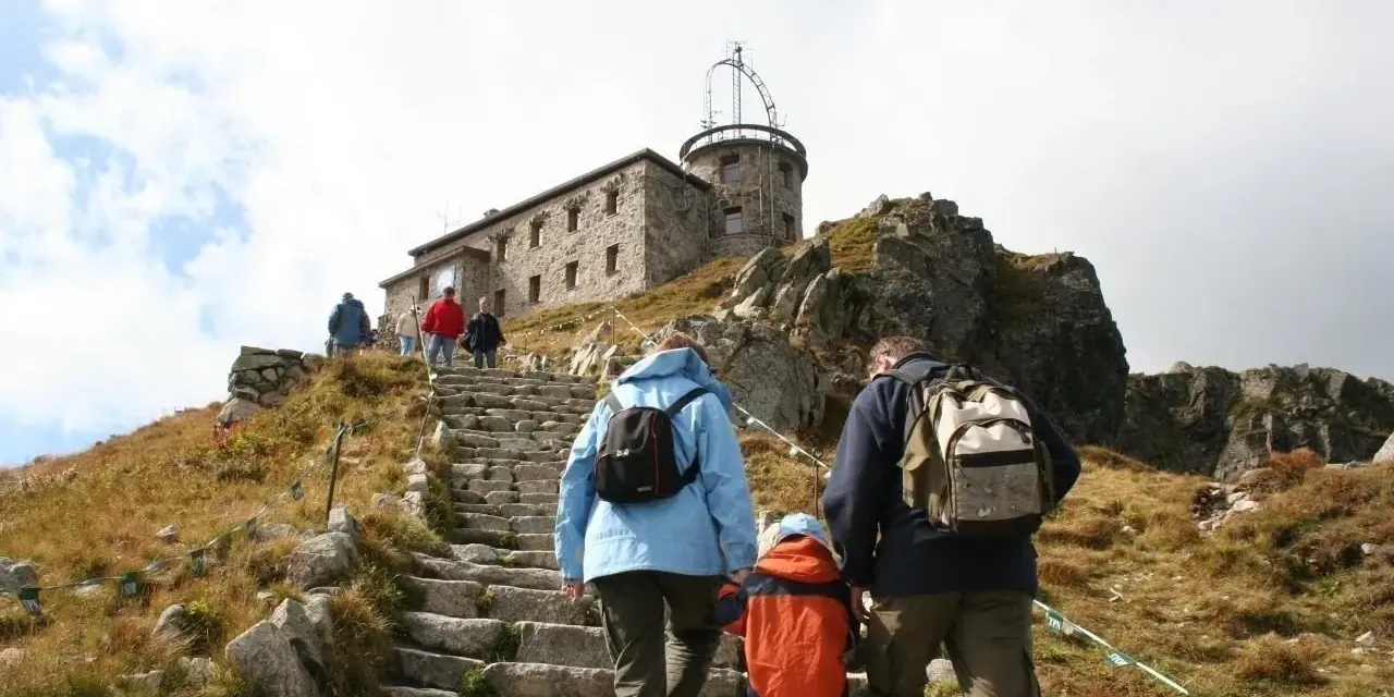 Rodzina wspina się kamiennymi schodami na Kasprowy Wierch. Na szczycie widać budynek obserwatorium.