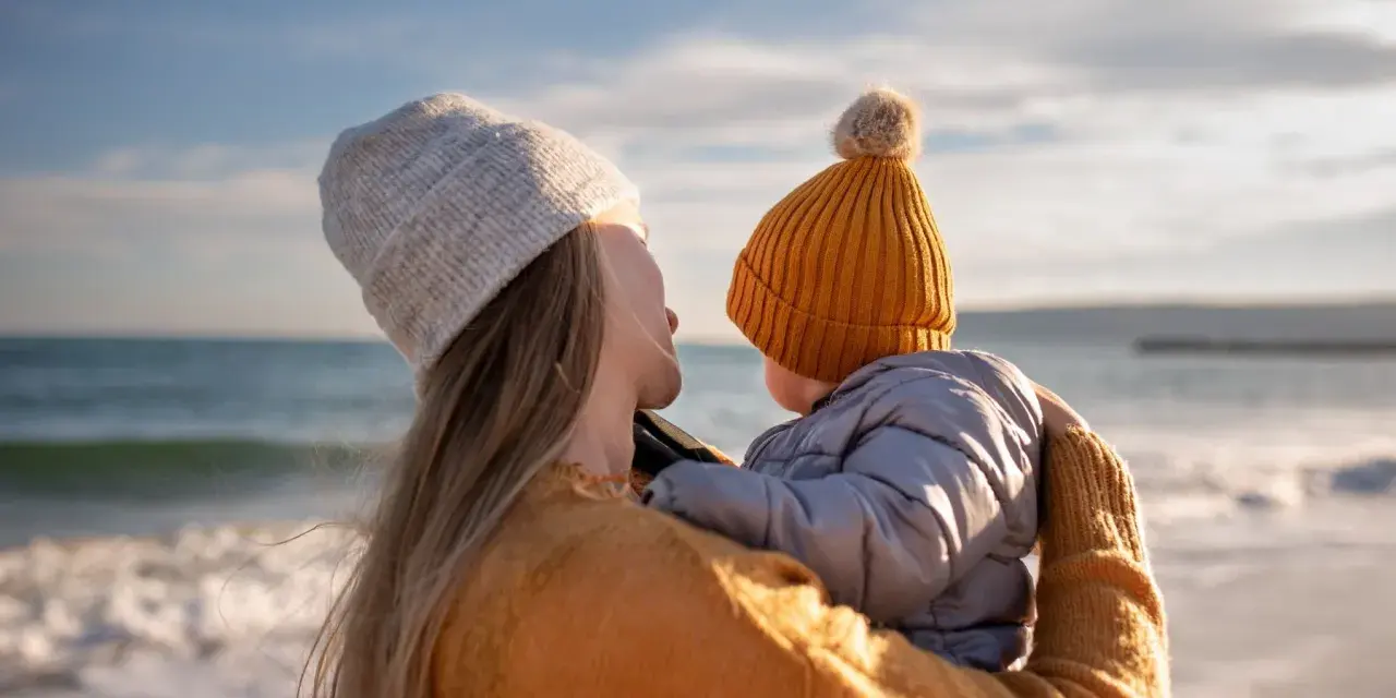 Madre abraza a su bebé en la playa, disfrutando de un momento de paz. Un respiro merecido, como una excedencia y vacaciones no disfrutadas, antes de volver a la rutina.