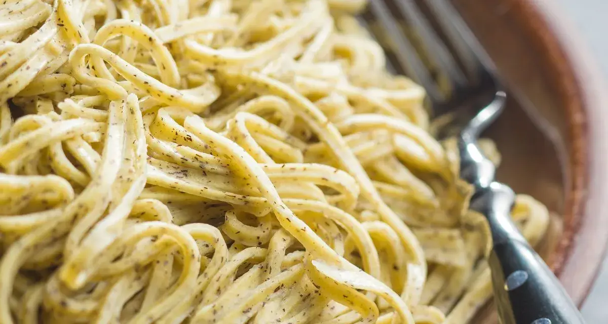 Un primo piatto invitante di tagliolini al limone, conditi con una salsa cremosa e profumata, pronti per essere gustati con una forchetta.