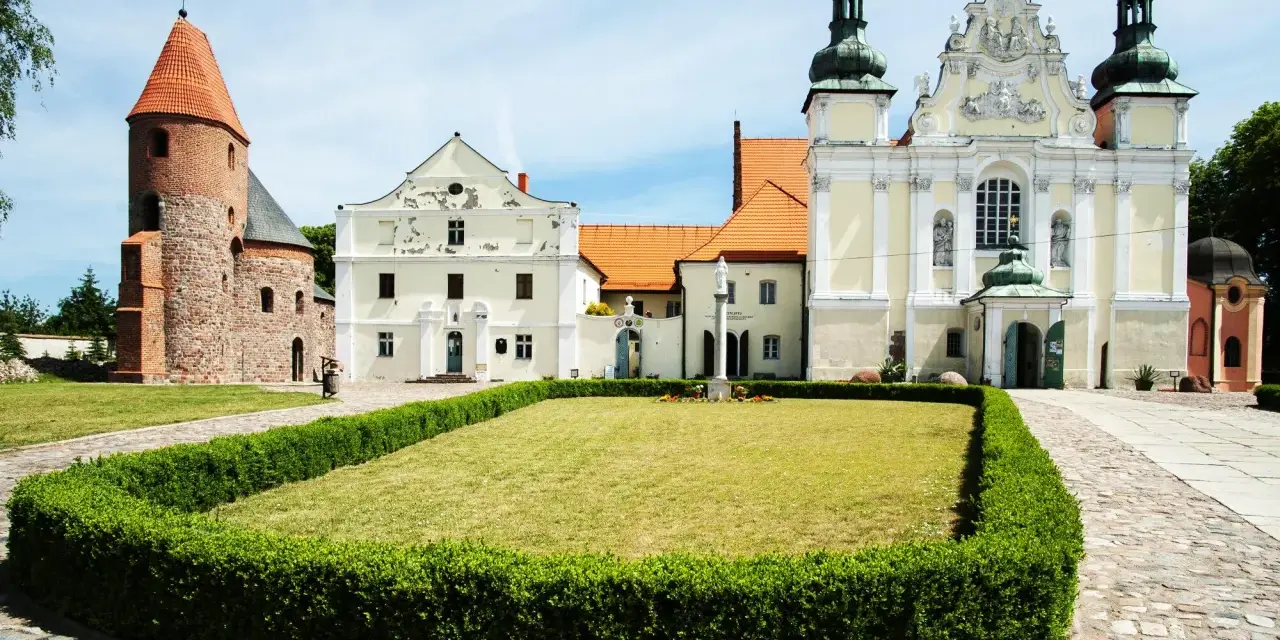 Kamienne kolumny w strzelnie otaczają trawnik przed barokowym kościołem i romańską wieżą.