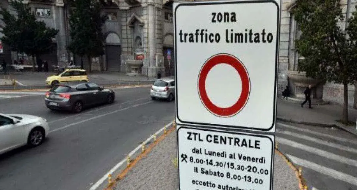 Cartello che indica "zona traffico limitato" con orari specifici. Auto in transito su strada urbana.