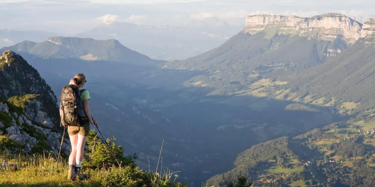Randonneuse contemplant un panorama grandiose lors d'une traversée de la Chartreuse. Les montagnes s'étendent à perte de vue.
