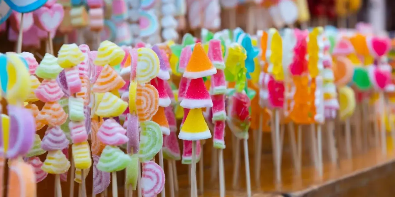 Coloridas manualidades con chuches en palitos, formando un arcoíris de dulces.