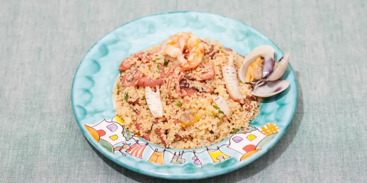 Un saporito cous cous di pesce con gamberi, polpo e cozze, servito su un piatto decorato.
