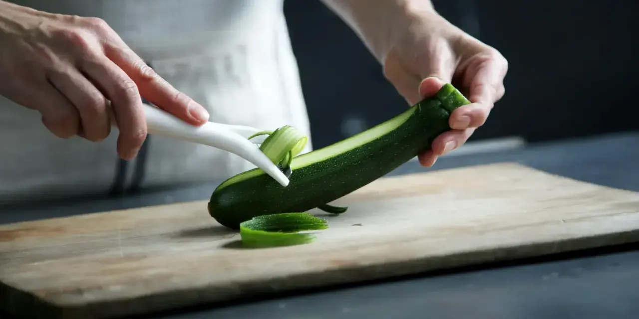 Manos pelando un calabacín para preparar deliciosas recetas con calabacín.