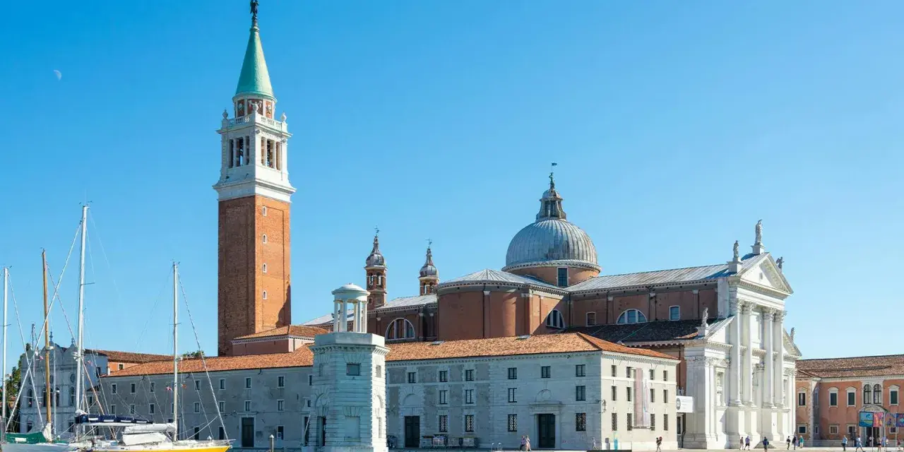 Il campanile di Venezia si erge maestoso accanto alla chiesa con la cupola, mentre barche a vela attendono sul canale.