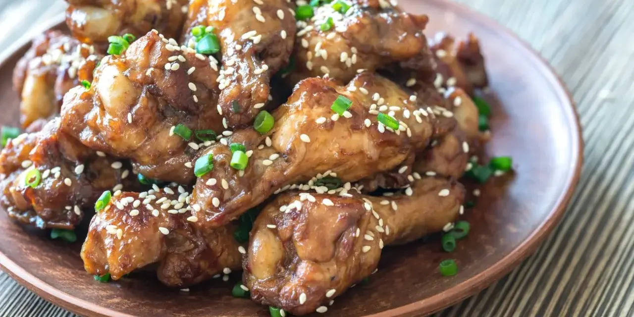 Alitas de pollo glaseadas con sésamo y cebolleta en un plato marrón.