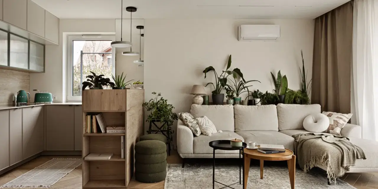 Minimalistyczne wnętrza z dużą ilością zieleni. Jasna kanapa, drewniane meble i kuchnia w neutralnych kolorach tworzą przytulną atmosferę.